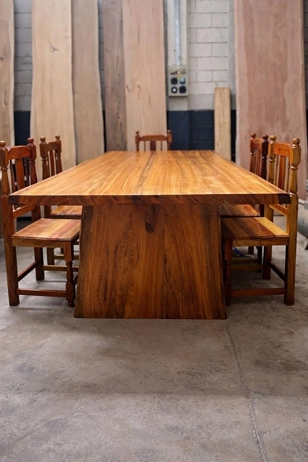 Mesa de tablón macizo con sillas, frente a tablones en el taller